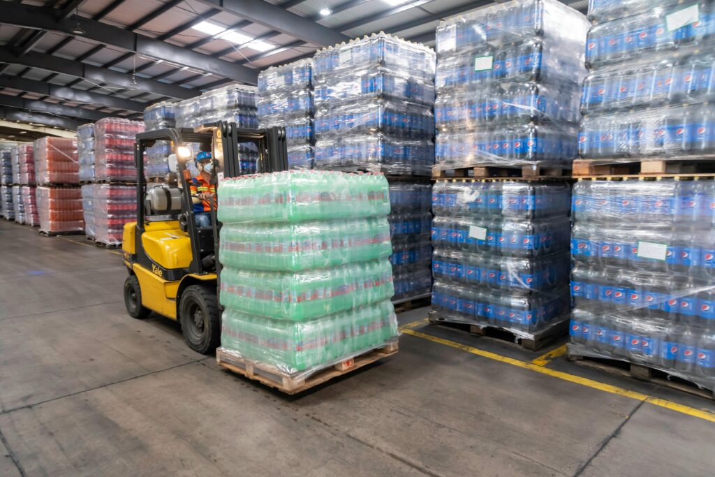 Empilhadeiras industriais movimentando pallets em um armazém organizado da Triunfo Foods, destacando a eficiência logística na distribuição de produtos alimentícios.